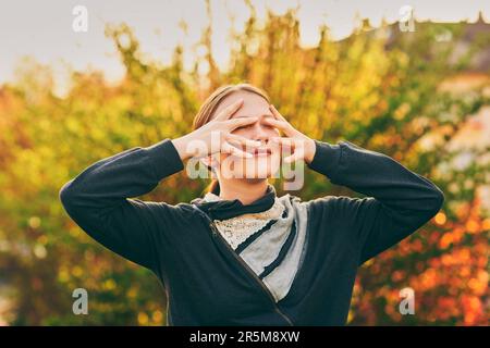 Outdoor portrait of young teen girl in golden light, hiding face with hands Stock Photo