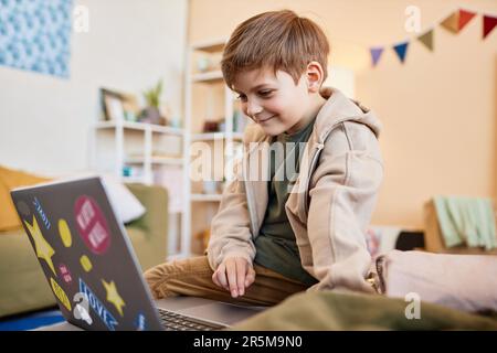 Side view portrait of smiling boy looking at computer screen while using internet at home Stock Photo