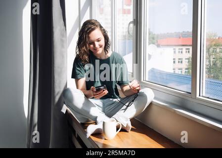 Modern Lifestyle: Woman Using Smartphone at Home - Female Student Engaged in Communication, Work, and Study, Embracing the Convenience of Mobile Apps Stock Photo