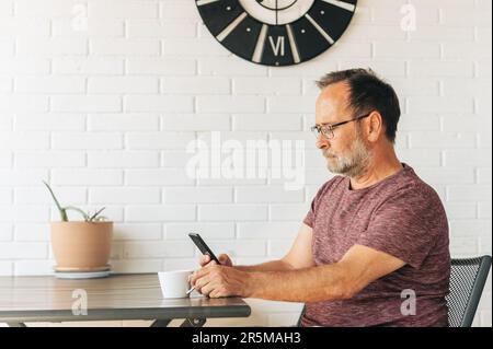 Middle age man relaxing on balcony, drinking cofee, using smart phone Stock Photo