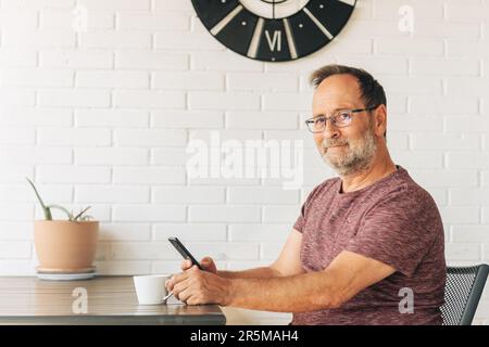 Middle age man relaxing on balcony, drinking cofee, using smart phone Stock Photo