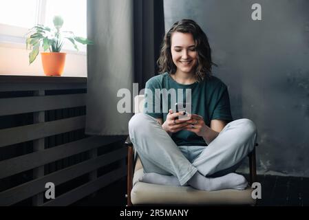 Digital Lifestyle: Young Woman Engages in Communication and Productivity Through Smartphone in the Comfort of Home. A Blend of Study, Work, and Connec Stock Photo
