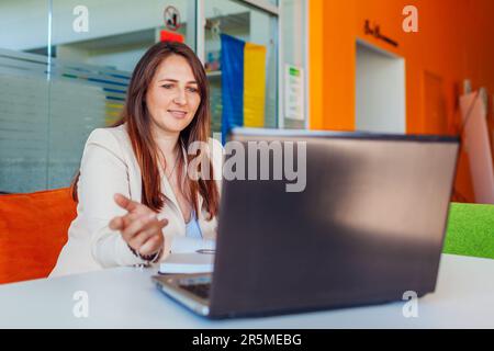 Young ukrainian teacher tutor talking to students in online chat through video conference calling on laptop by national blue and yellow flag. Working Stock Photo