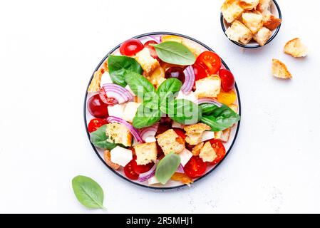 Panzanella italian vegetable salad with stale bread, colorful tomatoes, mozzarella cheese, onion, olive oil, salt and green basil, white table backgro Stock Photo