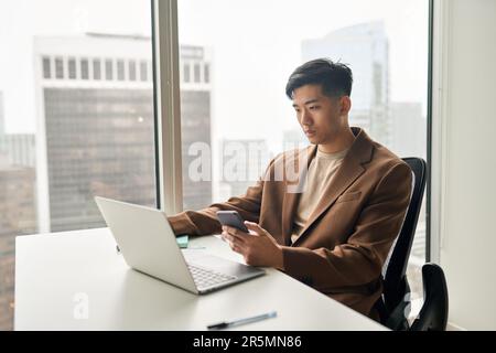 Young busy serious Asian business man using phone and laptop office. Stock Photo