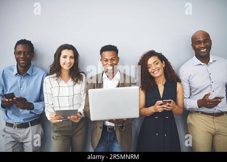 Wireless tech ensures we stay ready. Studio shot of a group of businesspeople using their wireless devices while waiting in line. Stock Photo