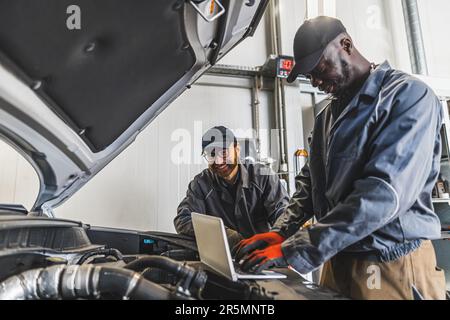 Two men mechanics completing car engine diagnostics with laptop in a repair shop. High quality photo Stock Photo
