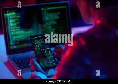 Seen from behind modern female with laptop and smartphone working on information security and encryption. Stock Photo