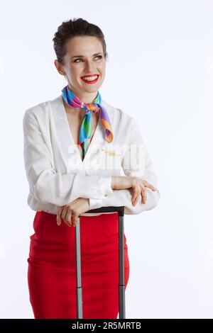 pensive elegant female air hostess against white background in uniform with trolley bag looking into the distance. Stock Photo