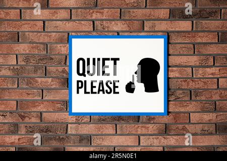 Quiet Please sign with shush gesture image on red brick wall Stock Photo