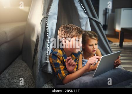 There is so much to browse online. an adorable little boy and girl using a tablet together while chilling in a homemade tent in the living room at Stock Photo