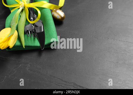 Cutlery set, painted egg and beautiful flower on black table, closeup with space for text. Easter celebration Stock Photo