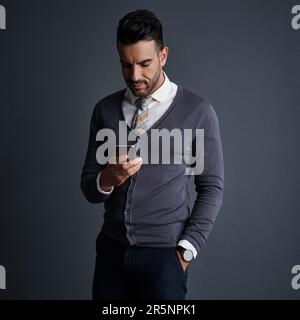 Getting work done in mobile format. Studio shot of a stylish young businessman using a mobile phone against a gray background. Stock Photo