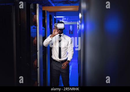 Experience the future of connectivity. a young man wearing a VR headset while working in a server room. Stock Photo