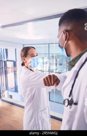 Safe greetings. two unrecognizable doctors wearing masks and elbow bumping while standing in the hospital. Stock Photo