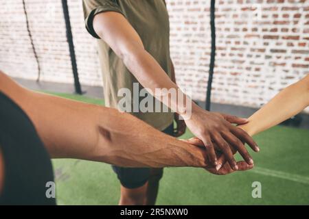 Make the most of your gym membership by joining a fitness group. three sporty young people joining their hands together in a huddle. Stock Photo