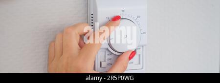 Woman hand adjusts or turns on wall temperature controller controller button Stock Photo