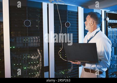 Building a strong network that can withstand any threat. a mature man using a laptop while working in a server room. Stock Photo