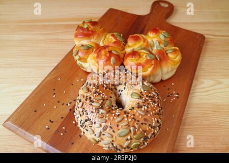 Closeup of delectable multi grains and sesame bagel and rolls on wooden breadboard Stock Photo