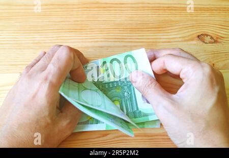 Man's Hand Holding a Bundle of 100 EURO Banknotes on Wooden Backdrop Stock Photo