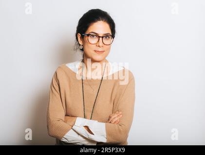Studio portrait of beautiful brunette woman, wearing glasses, arms crossed, posing on white background Stock Photo