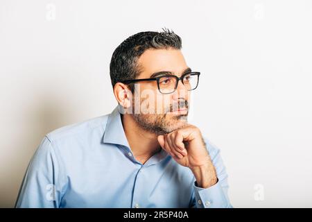 Studio portrait of handsome man wearing formal blue shirt and glasses, posing on white background, leaning on one hand, looking on the side Stock Photo