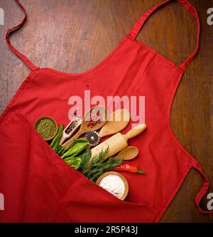 Baking background with red apron, rolling pin, herbs and kitchen utensils on a black background. View from above. Flat style. Stock Photo