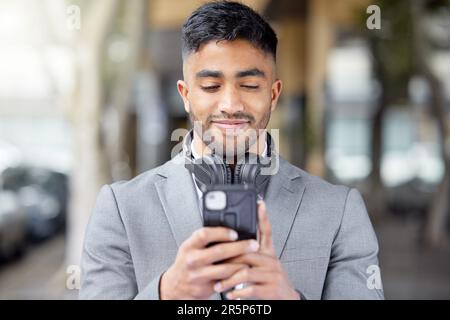 Business man, phone and city of a professional with headphones watching a video. Urban, smile and Indian male person with work travel, mobile Stock Photo