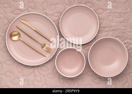 A set of cream color plates of different sizes on table, top view. Golden cutlery and serving utensils. An empty dishes on a light beige fabric tablec Stock Photo