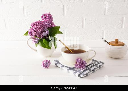 A cup of fragrant tea in the interior of the kitchen table with a bouquet of lilacs in a white jug. cottage. Tea ceremony Stock Photo