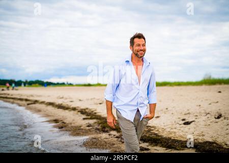 Handsome middle-aged man walking on the beach in summer Stock Photo