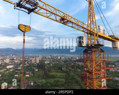 Close-up view from a drone of a construction crane cabin against the backdrop of beautiful mountains and sky. Construction concept Stock Photo