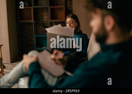 Two businesspeople working, the man is writing something on his note book and the woman is reading through the paper documents with the laptop in her Stock Photo