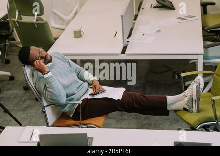 Sleeping at the office. Young black male is tired after hard daily tasks at work, so he took a nap Stock Photo