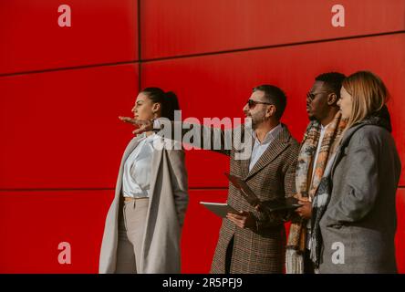 Close up of older business man showing something to his colleagues while standing next to the red building Stock Photo