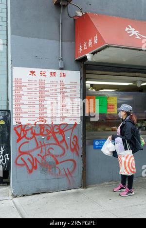 A Chinese woman wearing a mask browses a menu at a restaurant in Chinatown, Flushing, New York.winter, 20233, wears, wearing, mask, shopper, Stock Photo