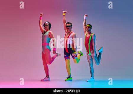Funny men in vintage, colorful sportswear posing, doing aerobics exercises  against gradient blue pink studio background in neon light Stock Photo -  Alamy