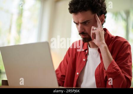 Pensive frowning man reading programming code on laptop screen Stock Photo
