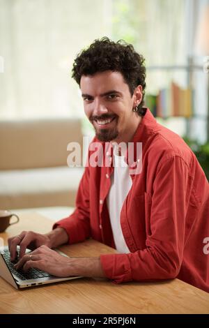 Portrait of smiling software developer working on laptop at desk in home office Stock Photo
