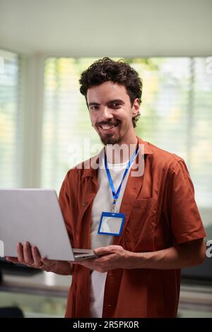 Portrait of happy programmer standing in office with opened laptop Stock Photo