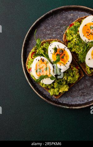 Sandwiches with rye bread and guacamole, with boiled eggs and microgreens of peas and radishes and sesame seeds, a plate with sandwiches close-up Stock Photo