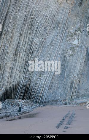 Tourists next to giant Flysh Cliffs on the Itzurun Beach in Zumaia, Basque Country, Spain Stock Photo