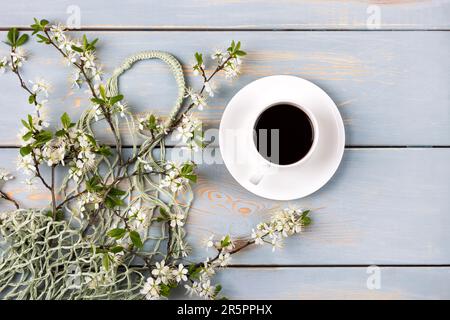 Shopping mesh string bag green with cherry blossom branches and cup of fresh black coffee on a wooden blue background with a place for your text. Flat Stock Photo