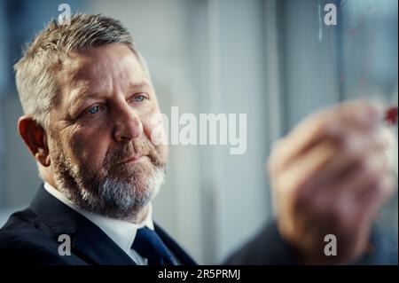 Hes the man with a business plan. a mature businessman having a brainstorming session against a glass screen in a modern office. Stock Photo