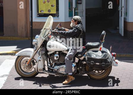Elderly male with a white beard on a Harley Davidson motorcycle, stopped at a crosswalk on the Santa Fe Plaza, Santa Fe, New Mexico, USA. Stock Photo