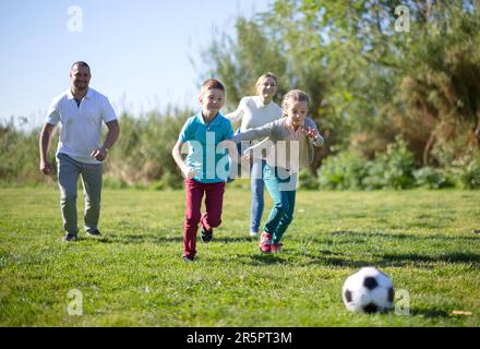 Father with mother with two children enjoy playing soccer on lawn in summer park Stock Photo