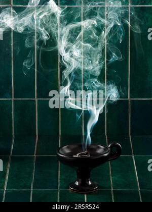Ceremonial Orthodox incense smoke ascending from black censer, on green tiles background Stock Photo