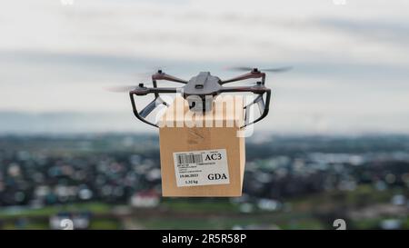 The drone is flying above city with a package for the customer - a close-up view of the device, the concept of drone delivery. Stock Photo