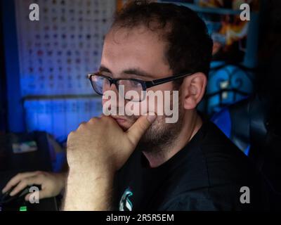 A young Caucasian man wearing glasses leaning on a desk while concentrated working on a computer Stock Photo