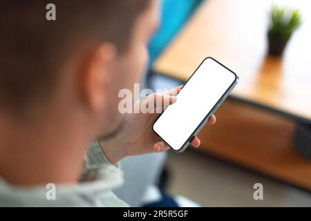 Man using smartphone with blank screen and frameless modern design while sitting on the sofa in home interior Stock Photo